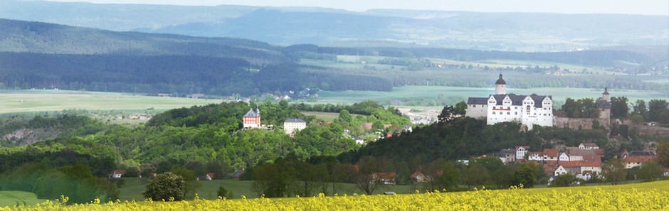 Blick über die Thüringer Landschaft mit bewaldeten Muschelkalkhöhen und Feldern. Auf einer Anhöhe thront ein barockes Schloss