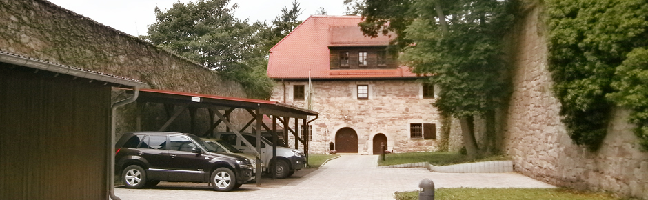 Historisches Forsthaus umrahmt von einer rustikeln mauer und grünen Laubbäumen